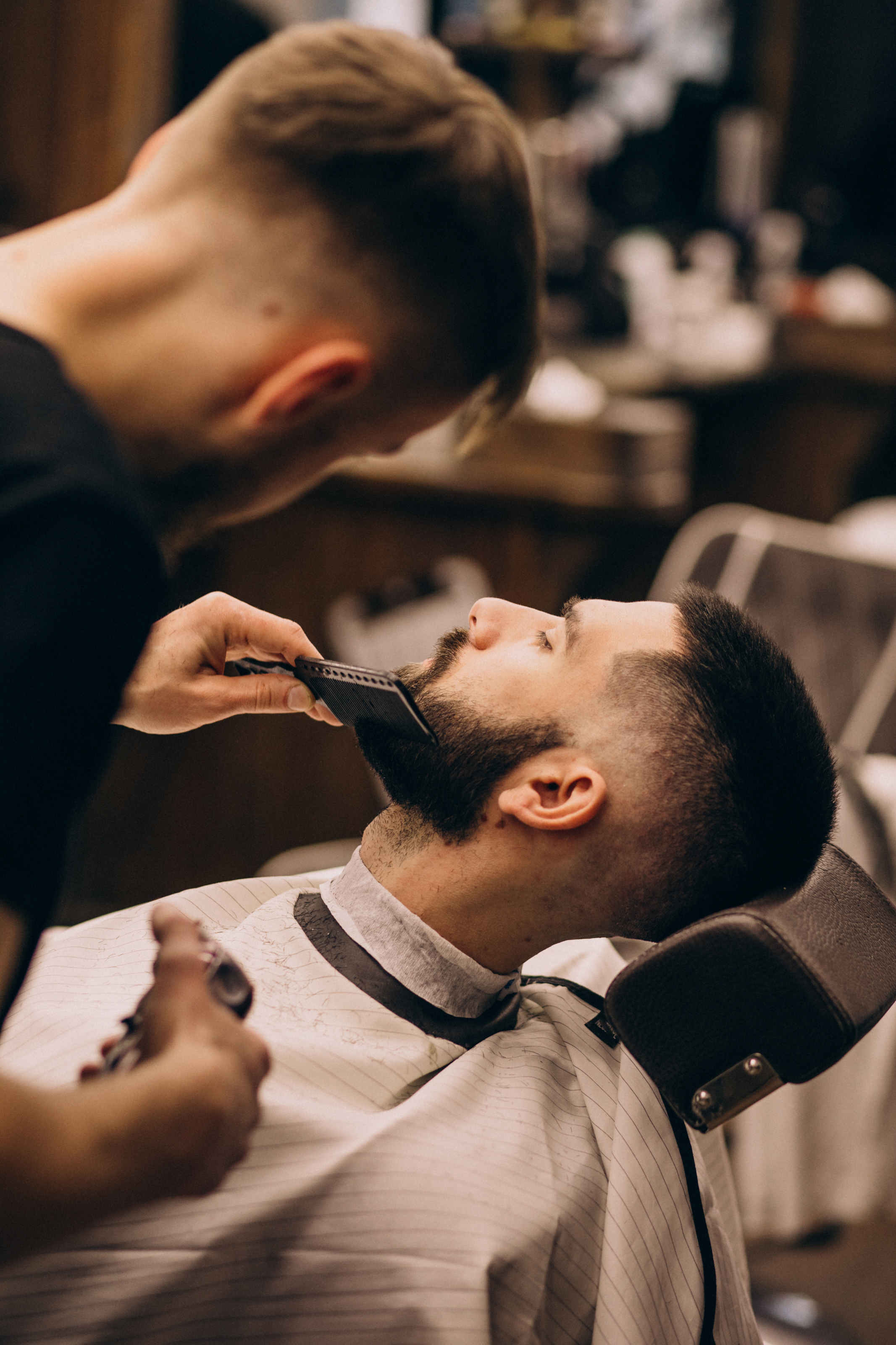 Un barbier soigne la barbe d’un client installé dans son fauteuil